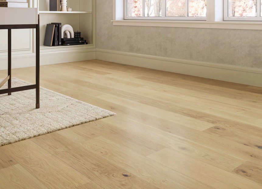 Light oak engineered hardwood floor in a bright room with a textured cream area rug, low-profile baseboards, built-in shelving, and a desk leg visible—showcasing flooring options for a home showroom, engineered hardwood, and flooring selection